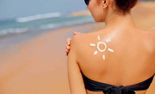 Young woman with sun shape on the shoulder holding sun cream bottle on the beach